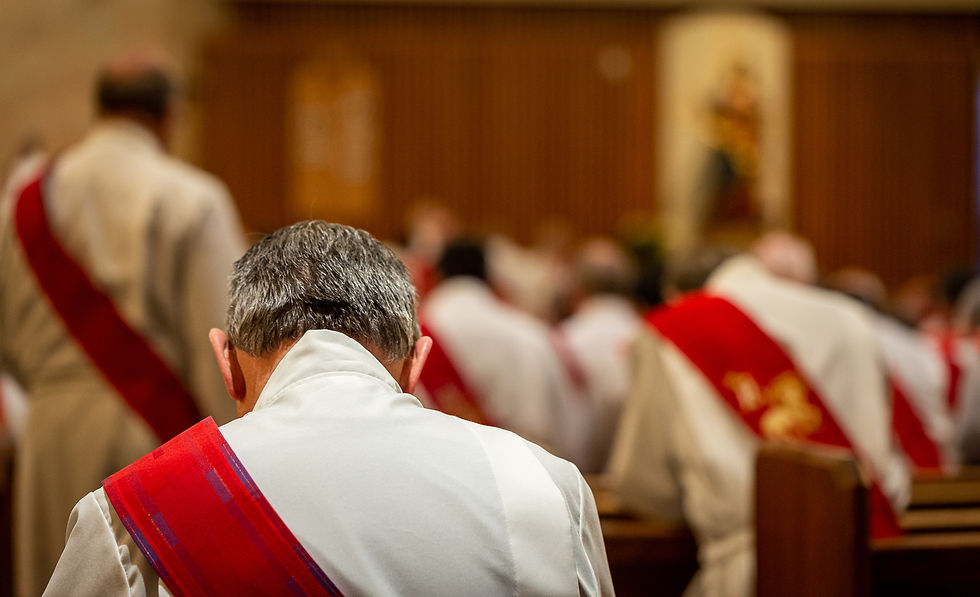A man with gray hair in a white robe and red stole praying in a church with other men